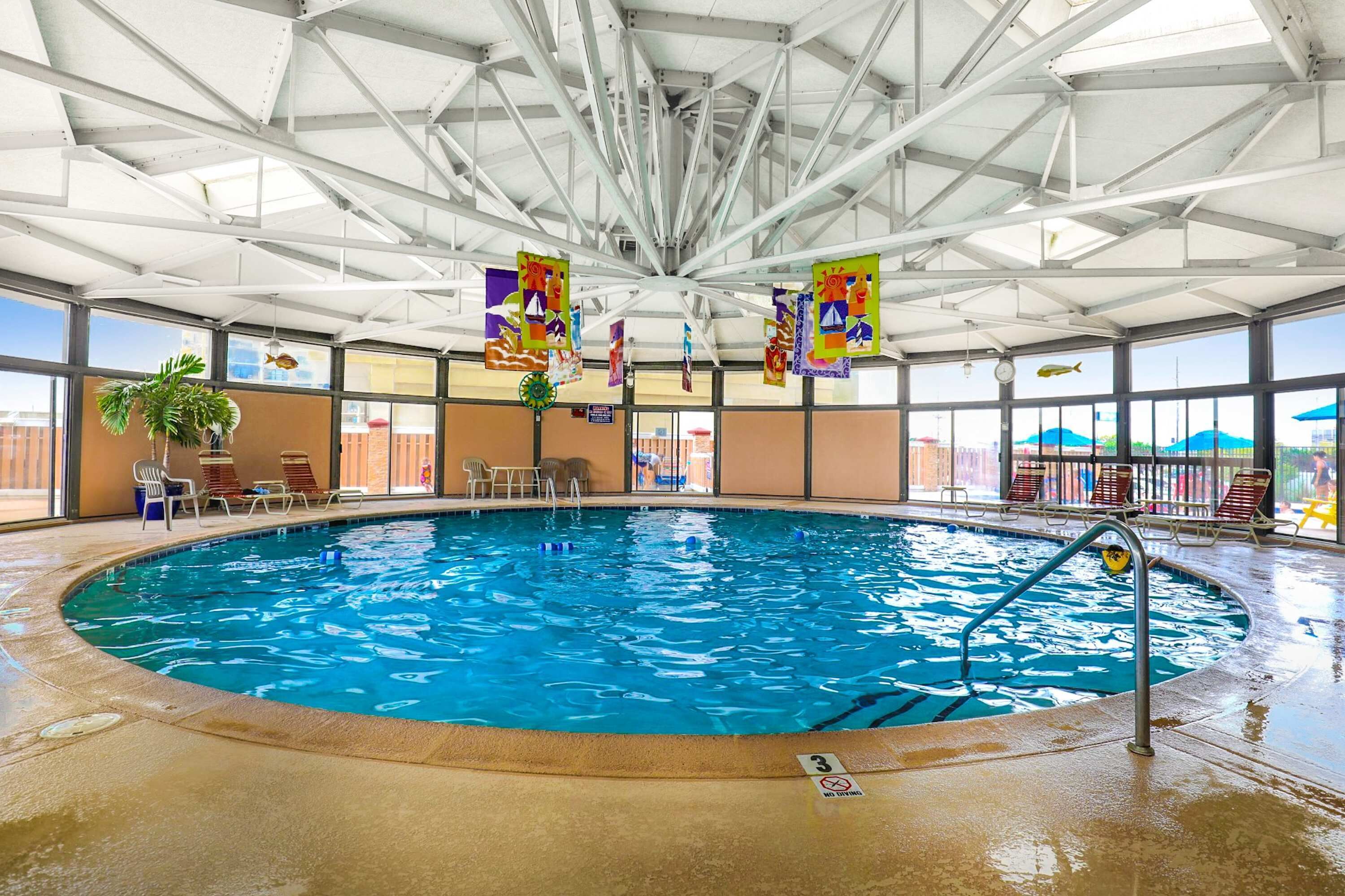 An indoor swimming pool with clear water, surrounded by lounge chairs and a high ceiling with metal beams.