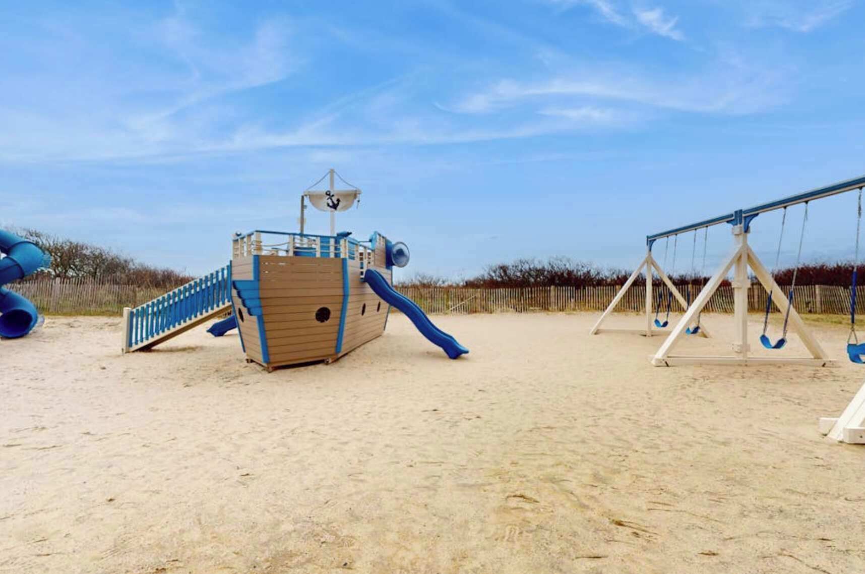 Une plage de sable avec une aire de jeux et des balançoires sur le thème des pirates.