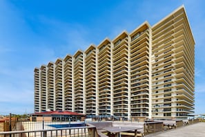 A high-rise hotel with multiple balconies, a pool area, and a boardwalk with seating. - Sea Watch 106- Oceanfront Escape with Pools, Arcade, Beach Access (Ocean City)