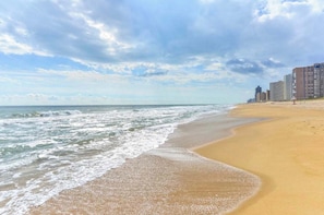 A beach with waves, a sandy shore, and buildings in the background. - Sea Watch 106- Oceanfront Escape with Pools, Arcade, Beach Access (Ocean City)