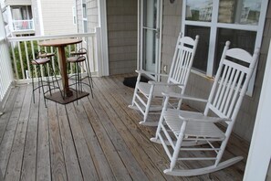 A wooden deck with a table and chairs, a white railing, and a window with a view of the outside. - 3 Pools ! Condo at Ocean Isle Beach by Williamson Realty (Ocean Isle Beach)