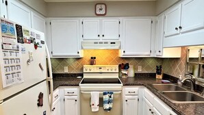 Una cocina con armarios blancos, una estufa, un refrigerador y un reloj en la pared.