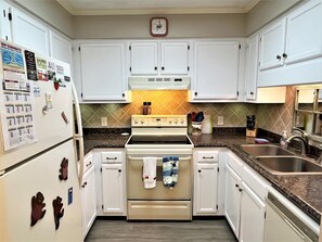 A kitchen with white cabinets, a stove, a refrigerator, and a clock on the wall. - 3 Pools ! Condo at Ocean Isle Beach by Williamson Realty (Ocean Isle Beach)