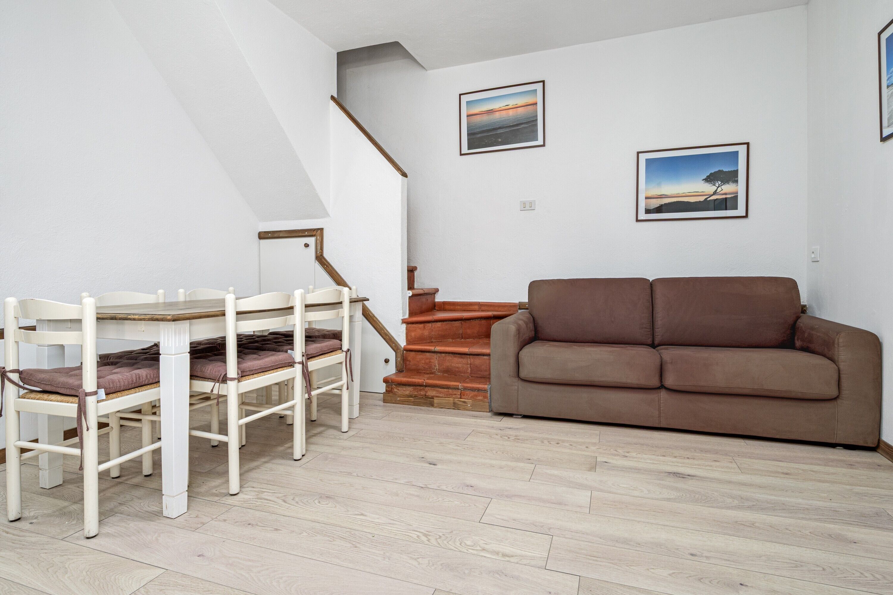 Une pièce comprenant une table à manger, des chaises, un canapé marron et un escalier.