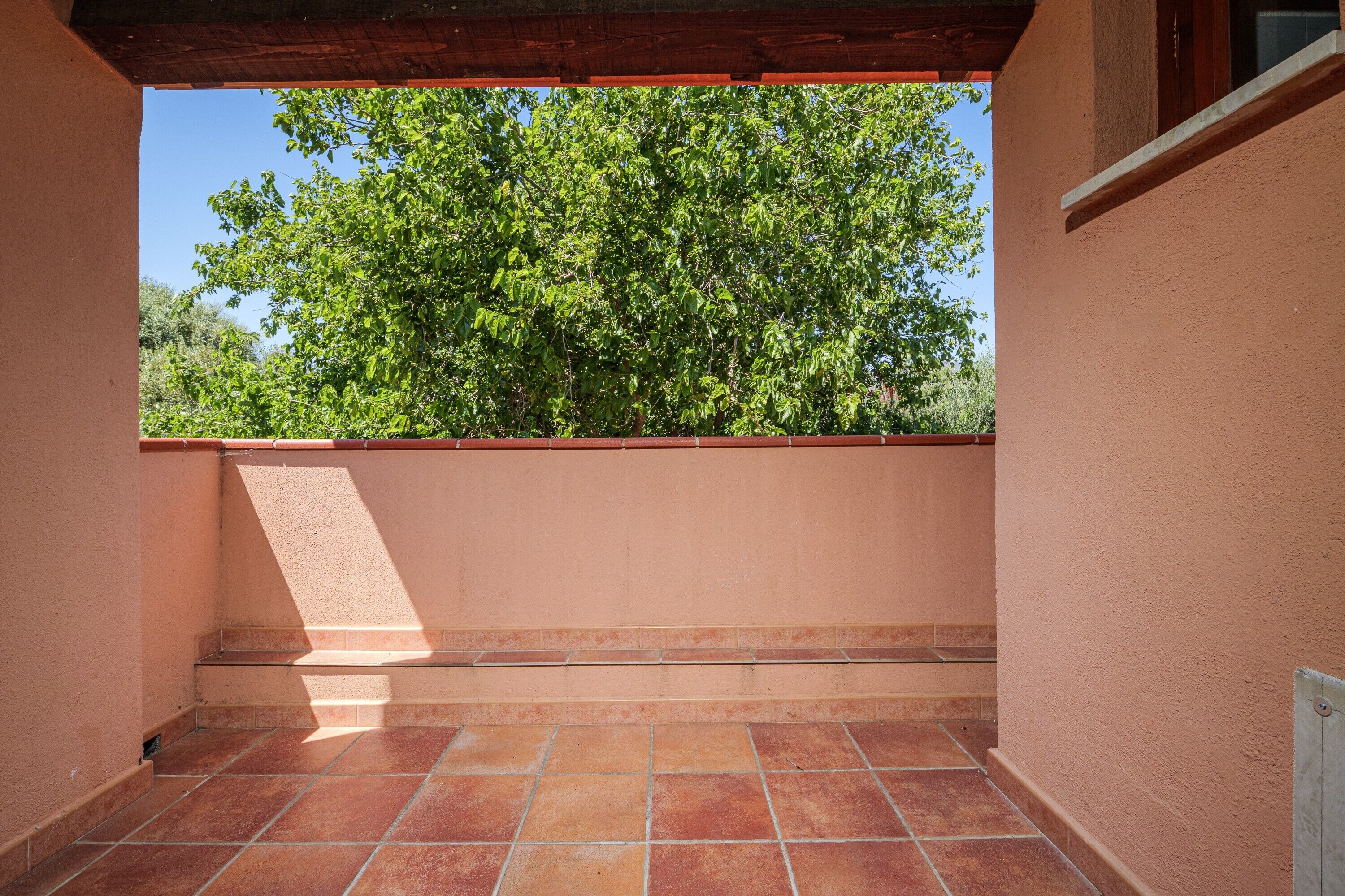 Un balcón con vistas a árboles verdes, suelo de baldosas y pared de color melocotón.
