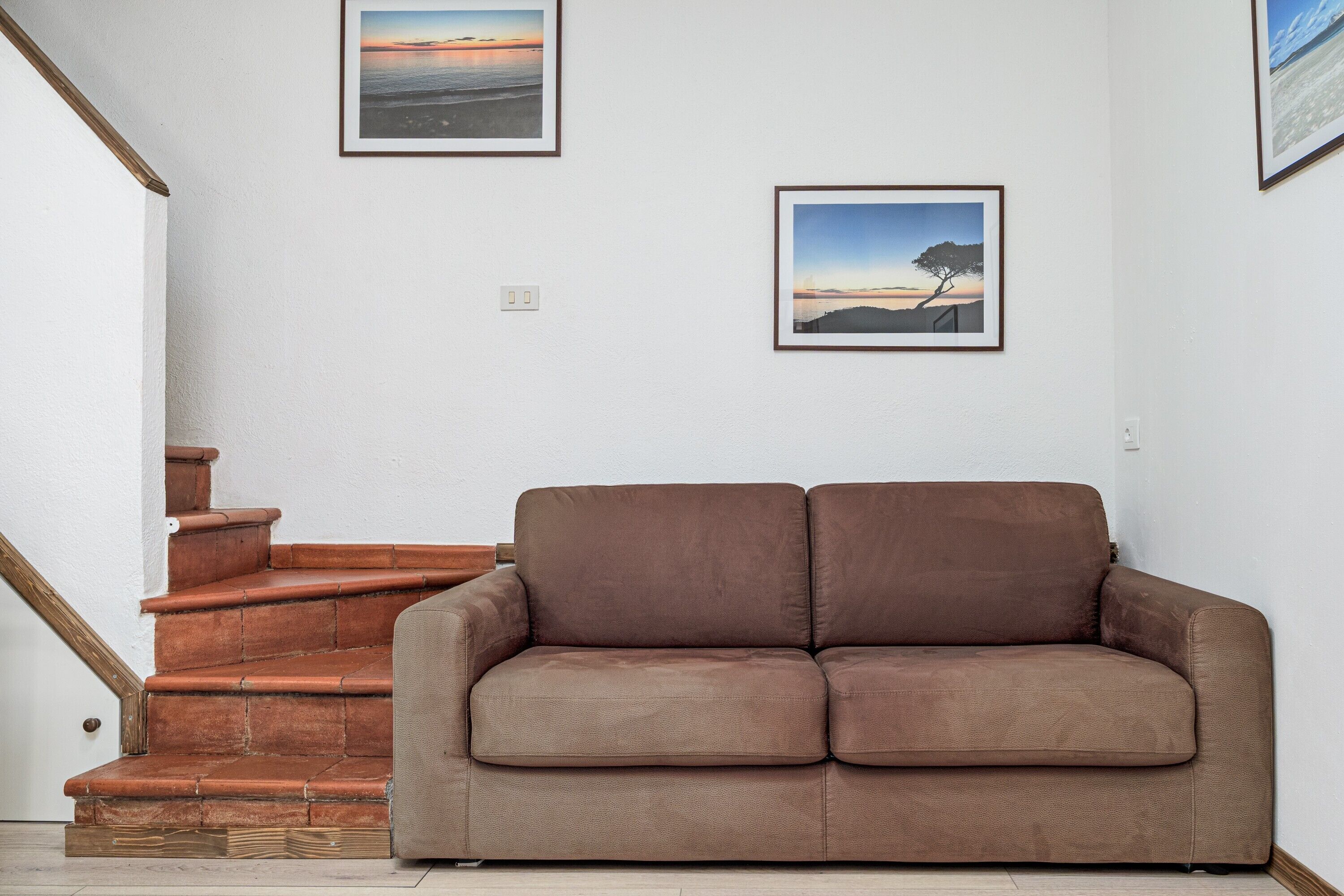 Ein braunes Sofa in einem Zimmer mit einer Treppe und zwei gerahmten Bildern an der Wand.