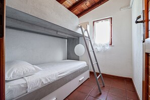 Una cama tipo litera con una escalera, una ventana con cortinas y un suelo de baldosas.