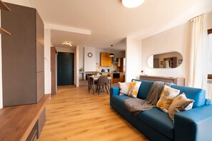 Ein modernes Wohnzimmer mit einem blauen Sofa, Holzboden und einer Küche im Hintergrund.
