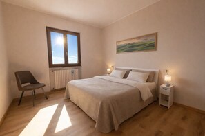 Ein Schlafzimmer mit einem Bett, einem Sessel, einem Nachttisch, einem Fenster und einem Bild an der Wand.