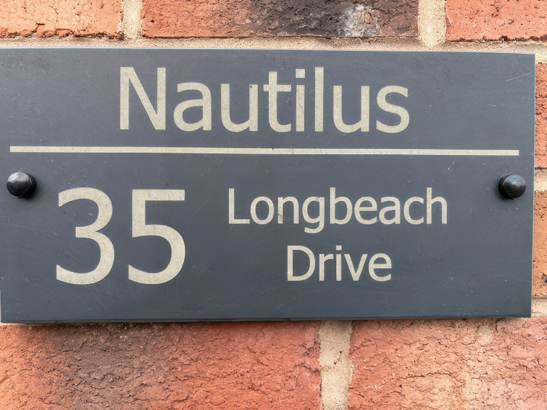 A house number sign for 'Nautilus 35 Longbeach Drive' mounted on a brick wall.