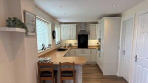 A modern kitchen with wooden countertops, white cabinets, and a central island with two chairs. - Nautilus (Chathill)