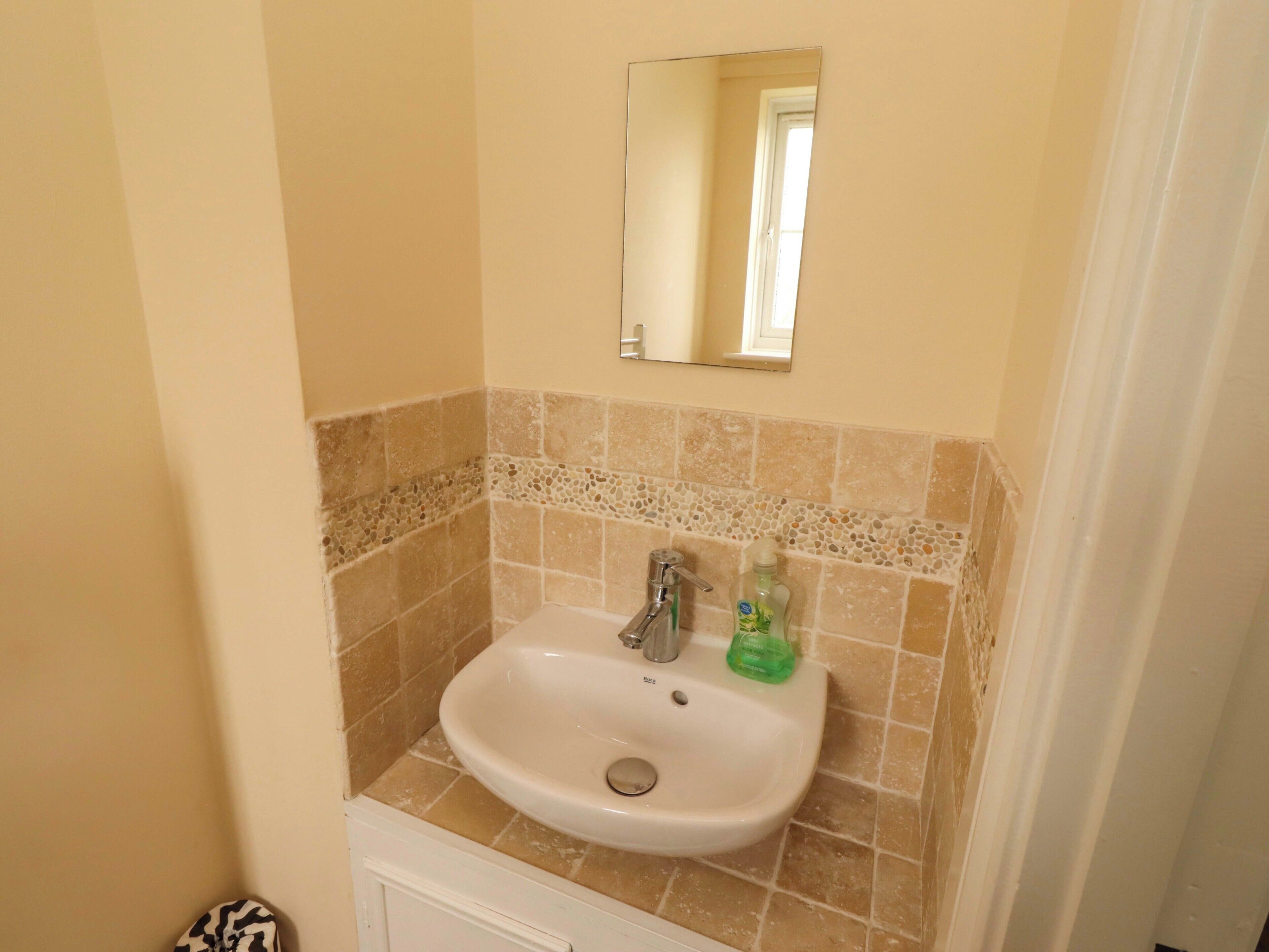 A bathroom with a white sink, a mirror above it, and a tiled wall.