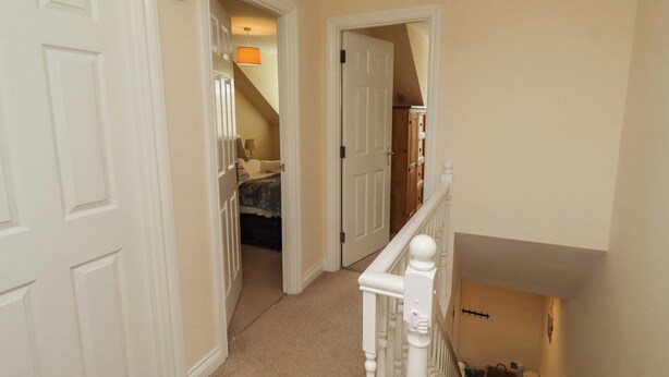 A hallway with a staircase, a door leading to a bedroom, and a hanging light fixture. - Nautilus (Chathill)