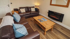 A living room with a brown leather sofa, patterned cushions, a wooden coffee table, a fireplace, and a framed picture on the wall. - Nautilus (Chathill)