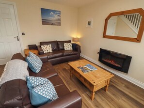 Ein Wohnzimmer mit braunem Ledersofa, gemusterten Kissen, einem Holztisch, einem Kamin und einem gerahmten Bild an der Wand.