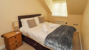 A bedroom with a bed, bedside tables, a lamp, a window with blinds, and a radiator. - Nautilus (Chathill)