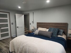 Ein Schlafzimmer mit einem Bett, einem Nachttisch, einer Lampe, einer Tür und einer Treppe.