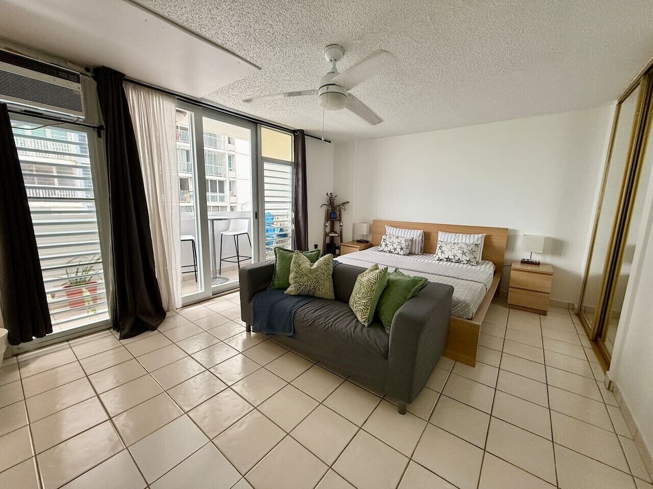 Une chambre moderne avec un canapé, un lit, une table de chevet, un ventilateur de plafond et une vue sur le balcon extérieur.
