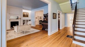 Un ampio soggiorno con pavimenti in parquet, camino, pianoforte e scala.