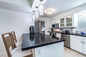 Eine moderne Küche mit einer schwarzen Kochinsel, weißen Schränken, Edelstahlgeräten und Pendelleuchten.