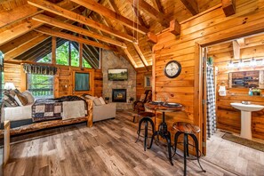 Ein gemütliches Blockhaus-Interieur mit Kamin, Essbereich und Wohnzimmer mit Sofa und Fernseher.