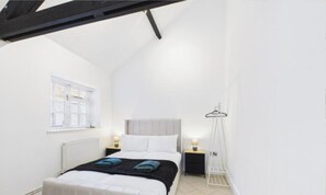 Ein Schlafzimmer mit Bett, Nachttischen, Heizkörper, Fenster und einer Kleiderstange.