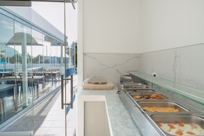 A buffet area with various food options, a glass partition, and a view of the outside. - Apartment Garden View 3 Guests with Wi-Fi and Air Conditioning (Αγ. Γεώργιος)