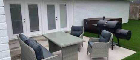Un patio con mobiliario de mimbre, una mesa y una parrilla.