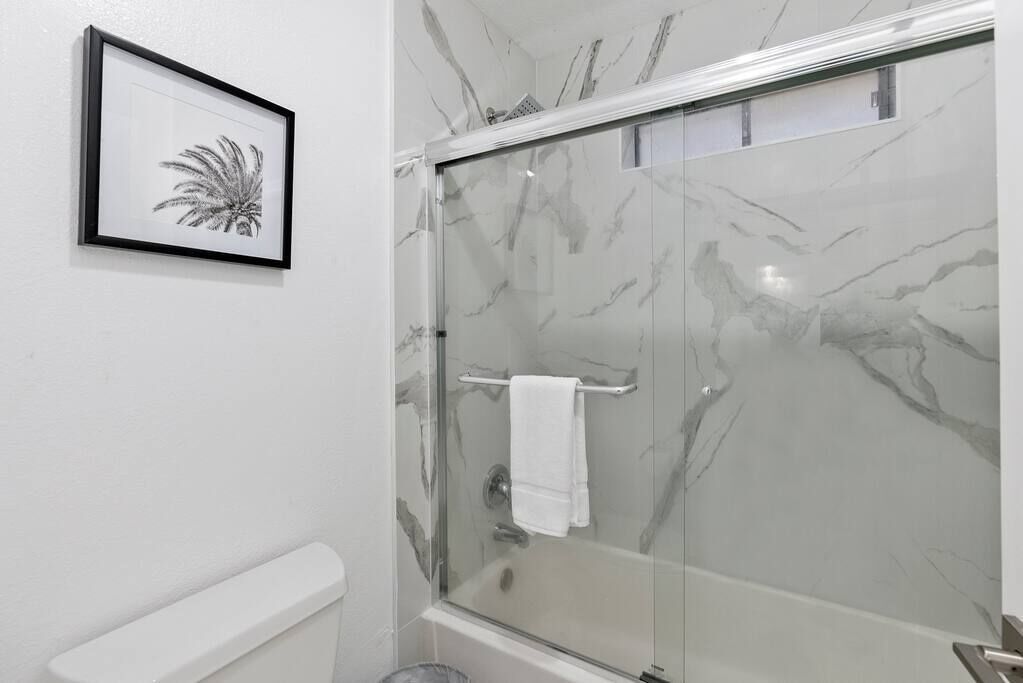 Ein Badezimmer mit Duschkabine aus Glas, einem gerahmten Bild an der Wand und einem weißen Handtuchhalter.