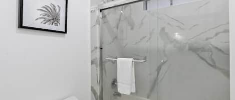 Ein Badezimmer mit Duschkabine aus Glas, einem gerahmten Bild an der Wand und einem weißen Handtuchhalter.