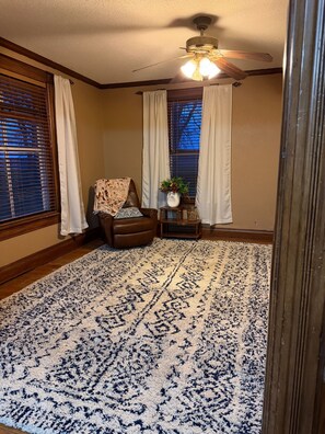 A room with a patterned rug, a brown leather chair, a ceiling fan, and a window with blinds.