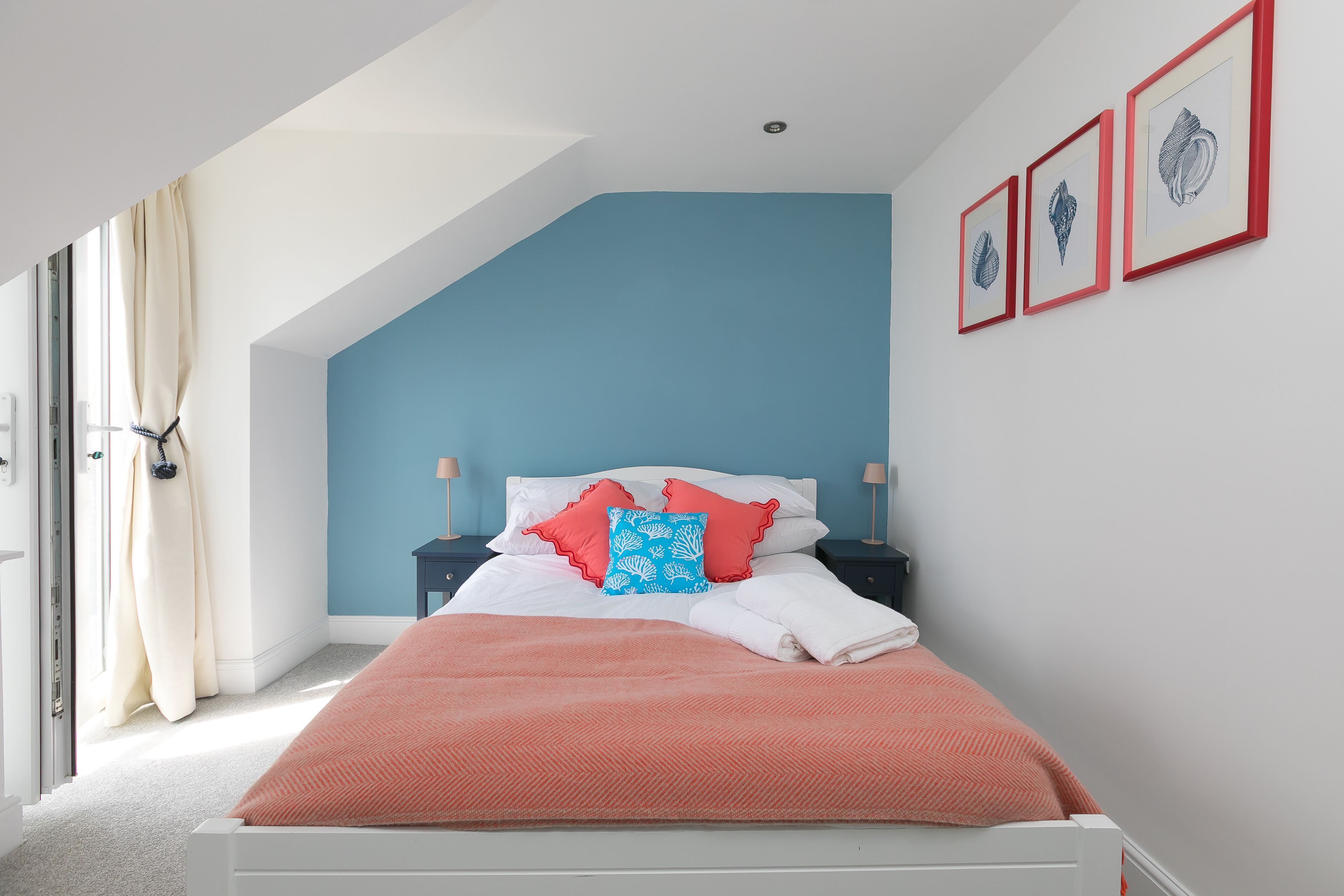 Une chambre à coucher avec un lit, un mur d’accent bleu, un plafond blanc et des œuvres d’art encadrées accrochées au mur.