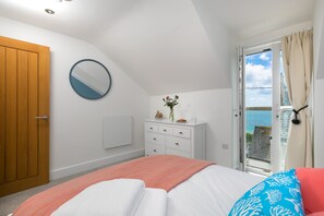 Ein Schlafzimmer mit Bett, Kommode, Spiegel, einem Fenster mit Vorhängen und Blick ins Freie.