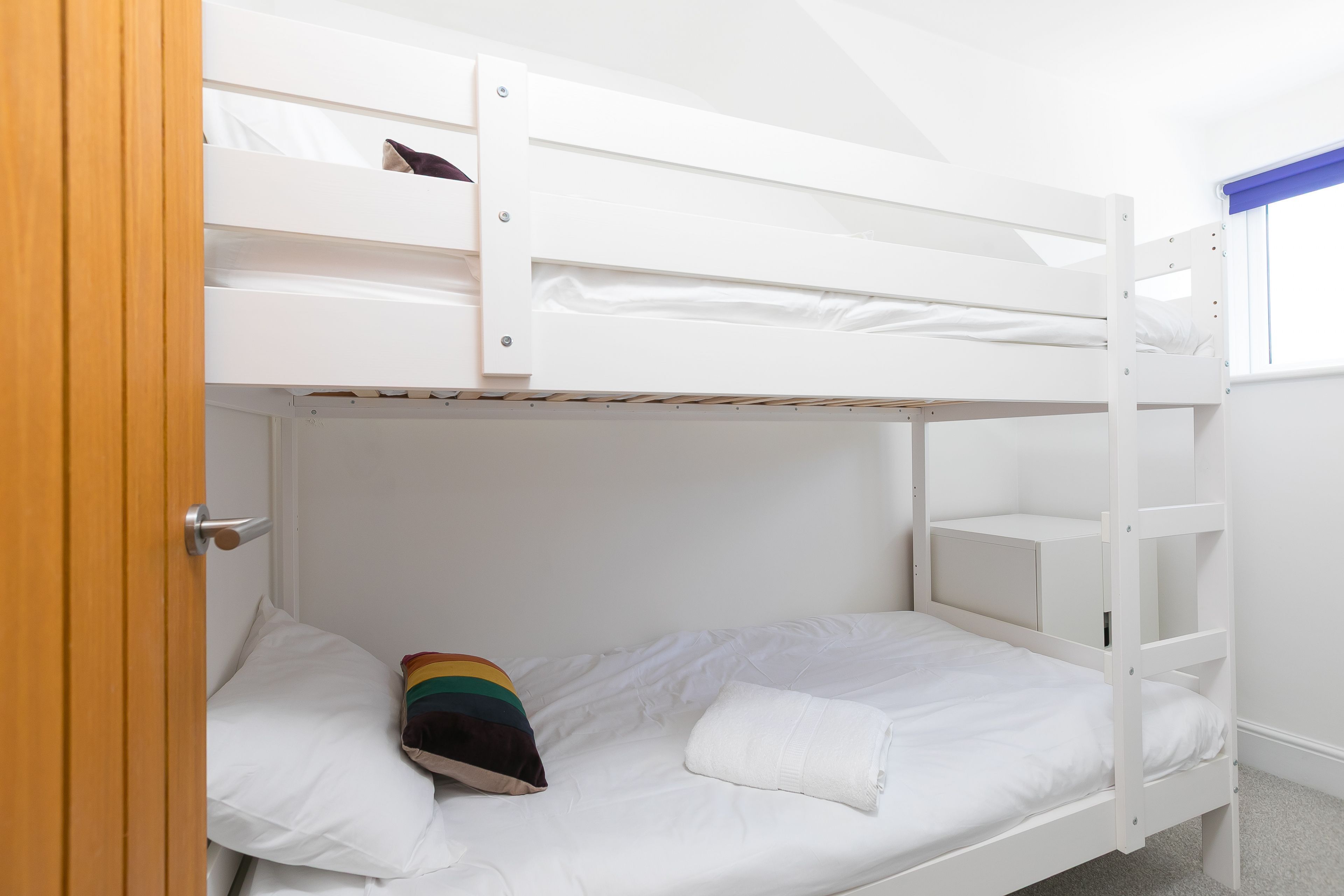 A bunk bed with a lower bunk, a door, and a window with blue blinds.