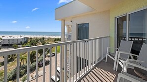 Ein Balkon mit Blick auf den Strand, weißen Stühlen und einem Tisch.