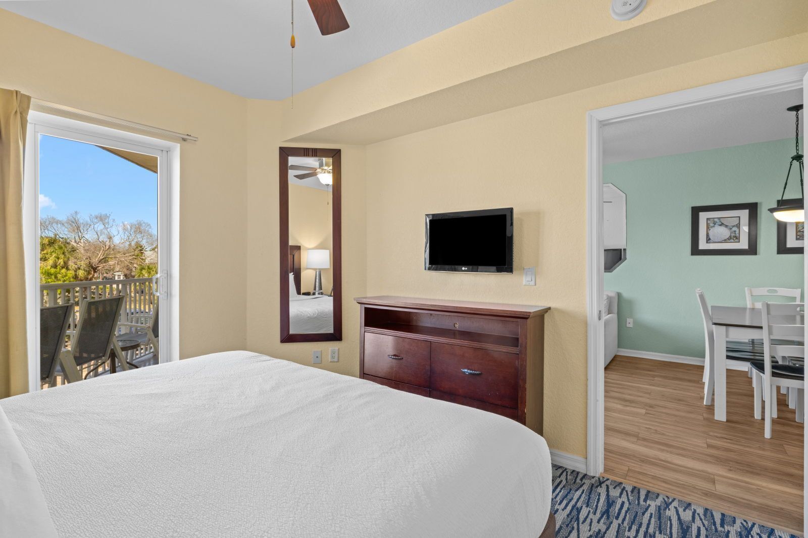 A hotel room with a bed, a TV, a dresser, a mirror, a balcony with chairs, and a dining area.