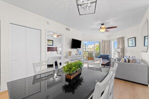 Un salon moderne avec une table à manger, des chaises blanches, un canapé gris, un téléviseur et un balcon avec vue.