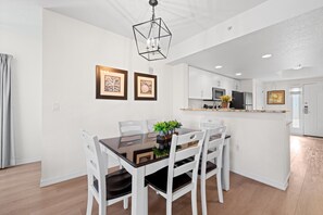 Une cuisine moderne avec des meubles blancs, un îlot central et un coin repas comprenant une table en verre et des chaises blanches.