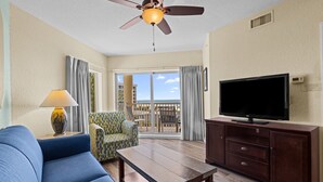 A living room with a sofa, a coffee table, a TV on a cabinet, a patterned armchair, and a ceiling fan. - Gulf View 2BR Suite Near Treasure Island Beach (Treasure Island)