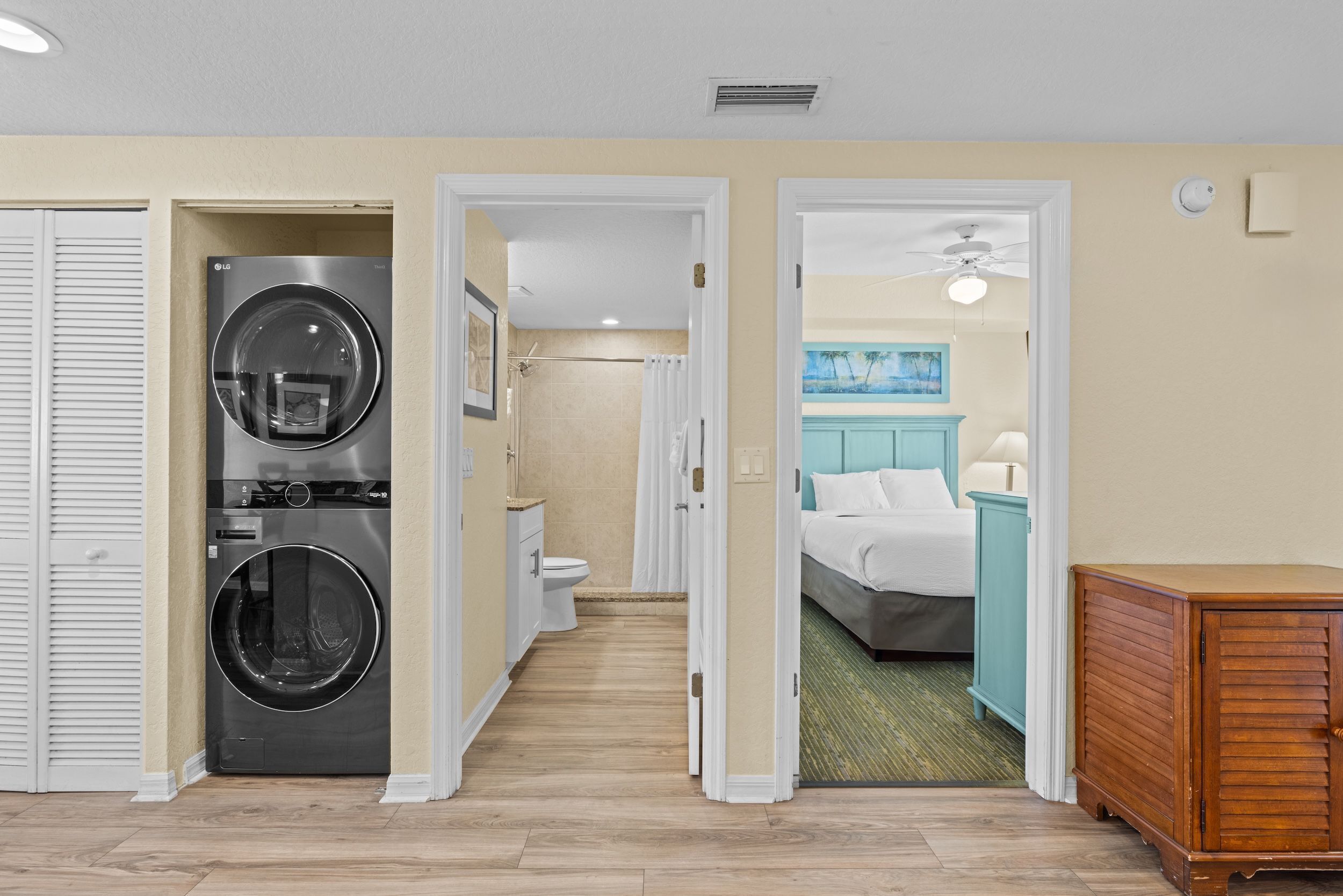 A hotel room with a washing machine, a bed, a bathroom, and a wooden cabinet.