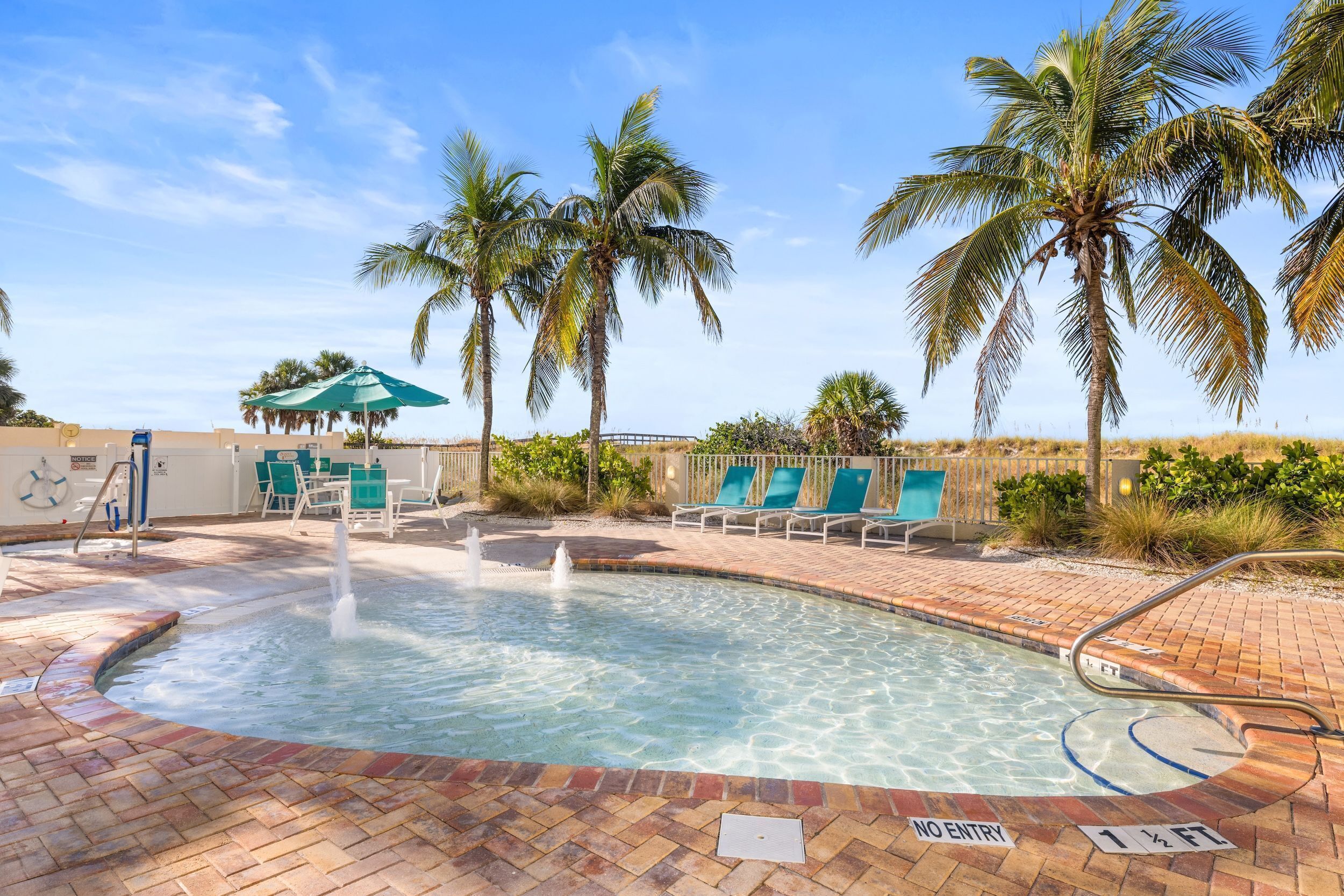 A swimming pool with palm trees, lounge chairs, and a no entry sign.