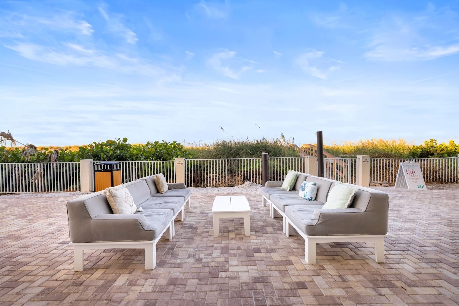An outdoor seating area with two sofas and a table, surrounded by a brick patio and a white fence.