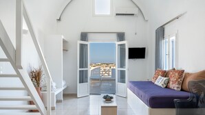 Un intérieur moderne avec un escalier, un canapé agrémenté de coussins, un téléviseur à écran plat et une vue dégagée sur l’extérieur grâce à une porte ouverte.