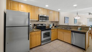 A kitchen with wooden cabinets, stainless steel appliances, granite countertops, and a dishwasher. - ADA Suite w/ Balcony & Beach Access (Treasure Island)