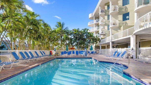 A swimming pool with lounge chairs, palm trees, and a multi-story building with balconies. - ADA Suite w/ Balcony & Beach Access (Treasure Island)