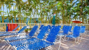 A poolside area with blue lounge chairs, a red and green pool table, and a white fence. - ADA Suite w/ Balcony & Beach Access (Treasure Island)