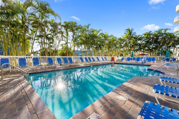 A swimming pool with blue chairs and palm trees.
