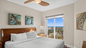 Ein Hotelzimmer mit einem großen Bett, einem Deckenventilator, Kunstwerken an den Wänden und einem Balkon mit Blick.