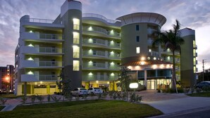 Ein mehrstöckiges Hotel mit Balkonen, ein Gebäude mit abgerundeter Ecke und ein Parkplatz.