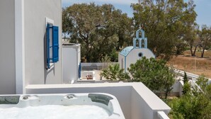 Un tetto con vasca idromassaggio, un edificio bianco con persiane blu e una chiesa sullo sfondo.